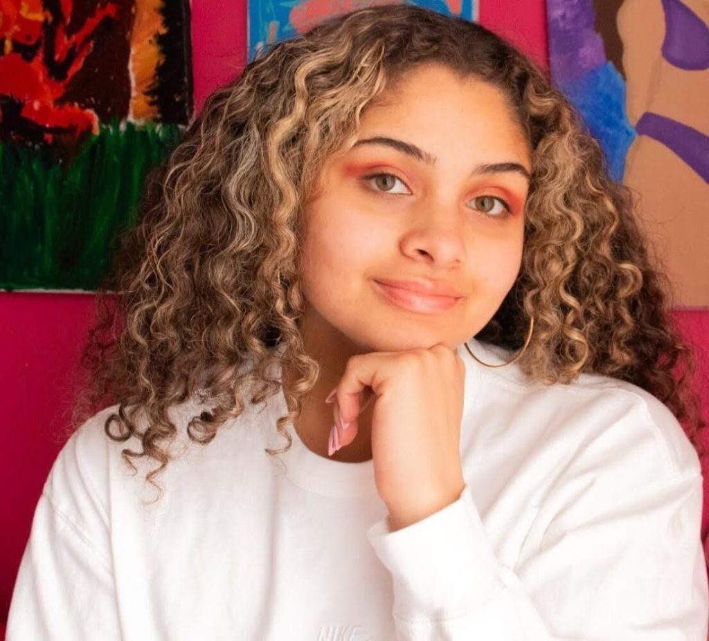 Photo of  Lauren Ortega in front of a red wall with art in the background.